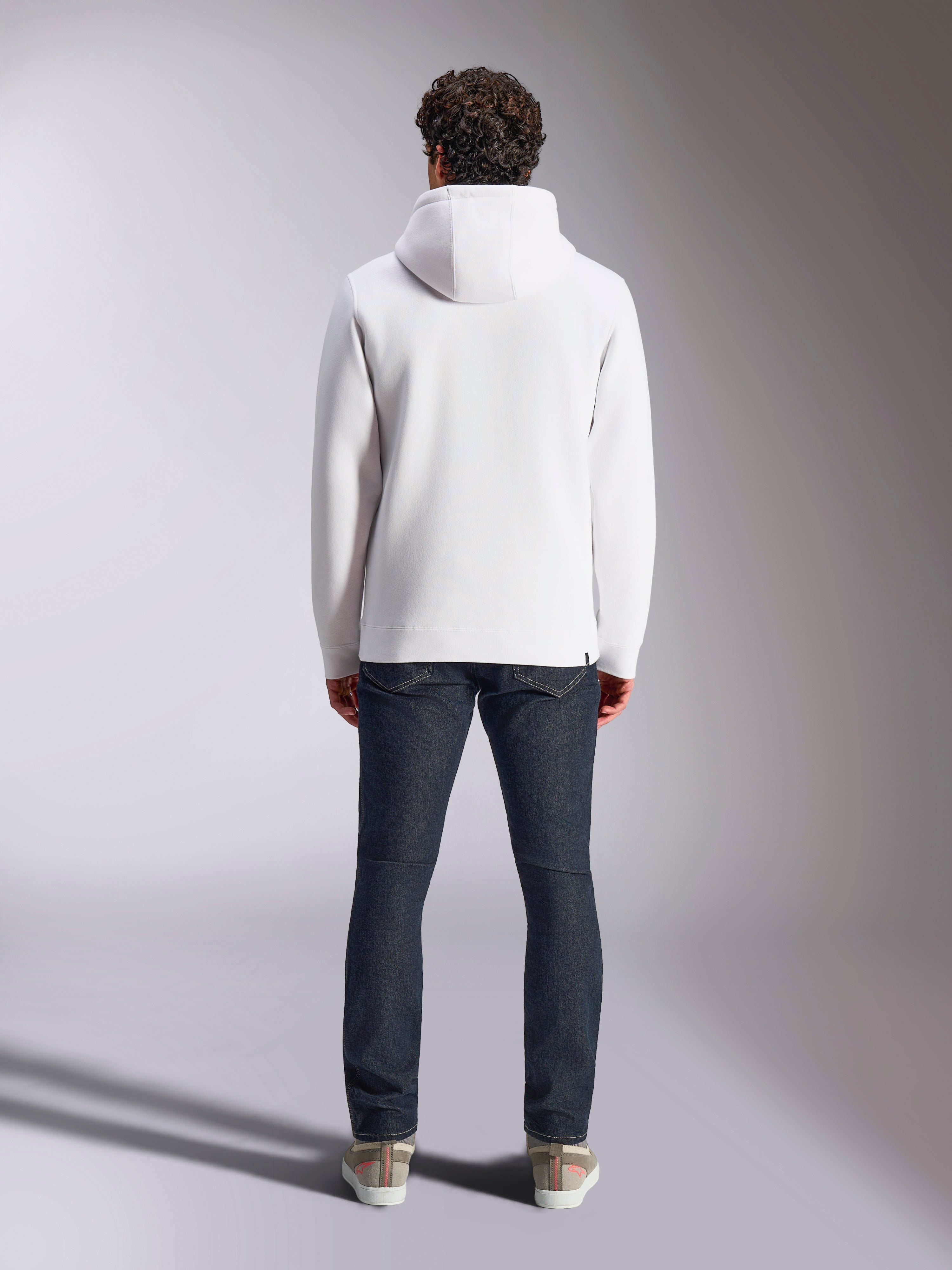 Sweat à capuche Alpinestars Blaze V3, hoodie blanc décontracté style sportswear, vue de dos du pull en polaire, design épuré avec poignets et ourlet côtelés, porté avec un jean bleu foncé et des baskets, vêtement lifestyle moderne inspiré du sport automobile