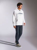 Sweat à capuche Alpinestars Blaze V3, blanc et bleu marine, tenue streetwear décontractée portée par un mannequin avec un jean bleu foncé et des baskets, comprend une capuche à cordon de serrage et un logo imprimé audacieux à l'avant, design moderne inspiré des sports mécaniques