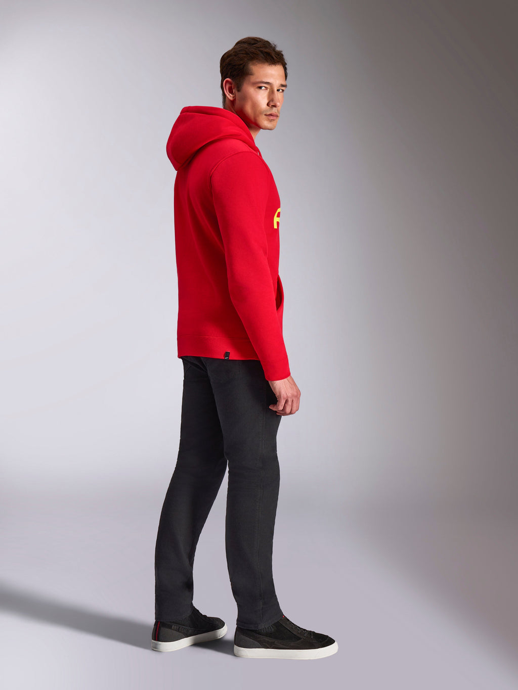 Sweat à capuche Alpinestars Ride V3, vêtement sportswear décontracté, rouge avec marquage jaune haute visibilité, modèle masculin portant un sweat à capuche rouge avec un pantalon noir et des baskets, vue de profil, modèle en polaire à enfiler avec poignets et ourlet en côtes