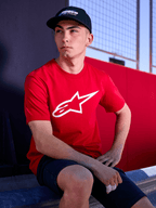 Casquette Alpinestars Profile noire, photo lifestyle d'un homme portant la casquette à visière courbée avec un t-shirt rouge arborant un logo Alpinestars blanc, style streetwear décontracté inspiré du sport automobile