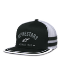 Casquette Alpinestars Backline Trucker, avant en sergé noir et dos en maille blanche, visière plate avec finition soutache blanche sur le bord, logo Alpinestars gris en arche avec mention Since 1963, bandes latérales appliquées, casquette snapback décontractée inspirée des sports mécaniques