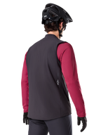 Gilet thermique Alpinestars A-Dura, noir, vue de dos, porté sur un maillot à manches longues bordeaux avec un casque de VTT et des gants noirs, équipement de cyclisme léger et isolé pour le tout-terrain