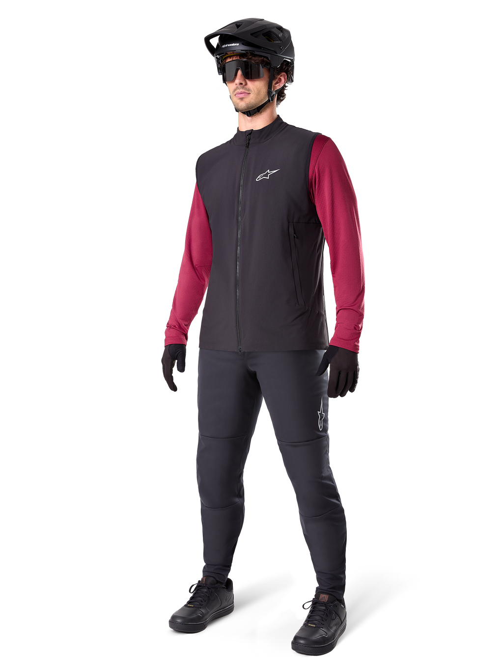 Gilet thermique Alpinestars A-Dura, gilet de cyclisme noir, porté par un cycliste par-dessus un maillot à manches longues bordeaux et un pantalon noir, avec un casque de VTT noir et des gants, conçu pour le VTT par temps froid
