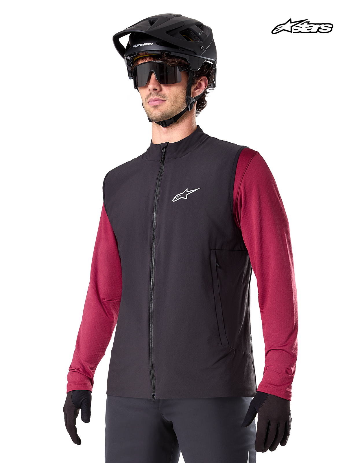 Alpinestars Gilet Thermique A-Dura, gilet de VTT thermique pour homme noir, porté par un modèle avec un casque et un maillot rouge à manches longues, isolation pour la pratique du VTT par temps froid