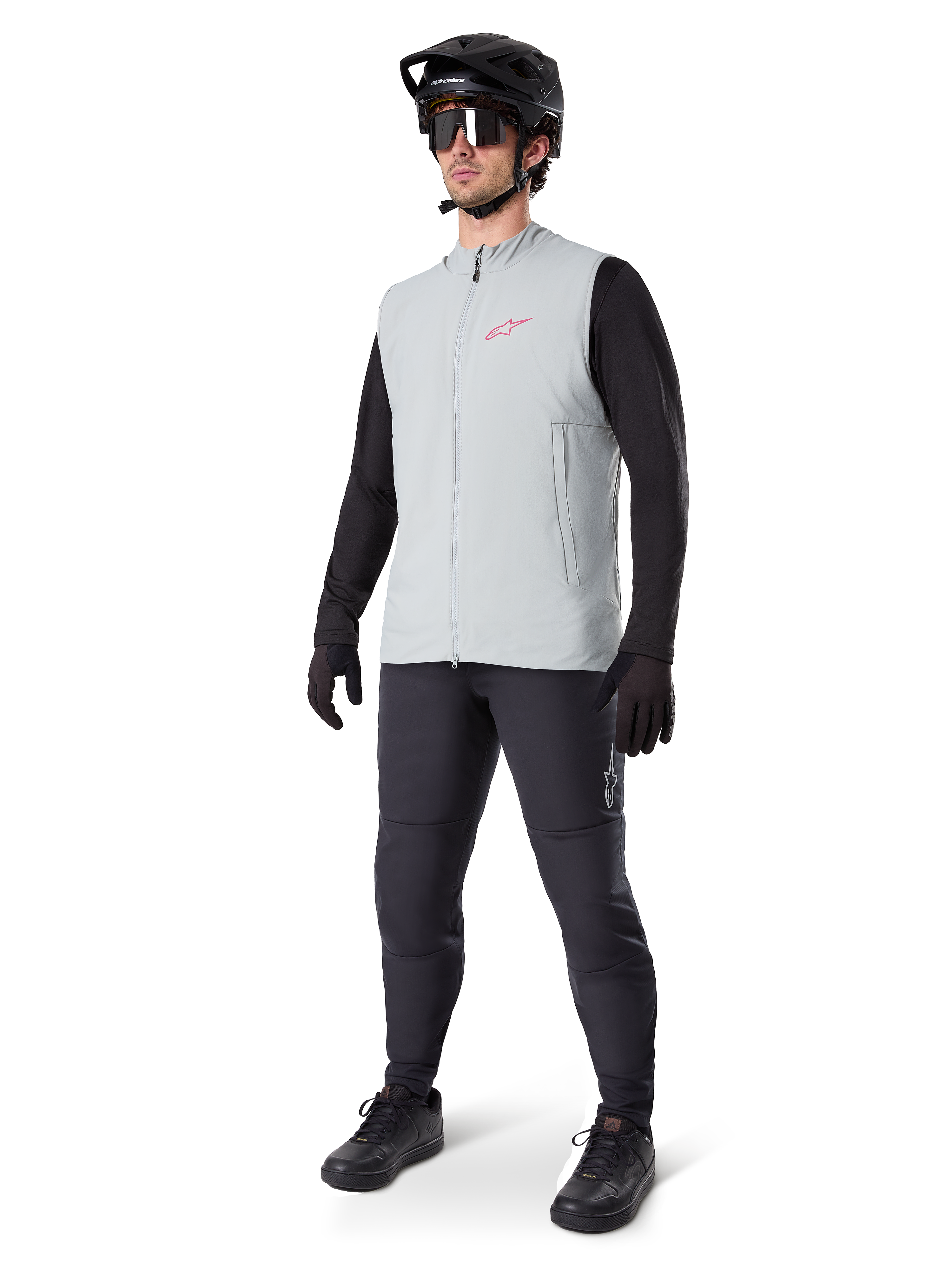 Alpinestars A-Dura Thermal Vest, Titanium gray cycling gilet with a pink logo, worn by a model with a black long-sleeve shirt, dark gray pants, and a black mountain bike helmet, performance gear for cold-weather riding