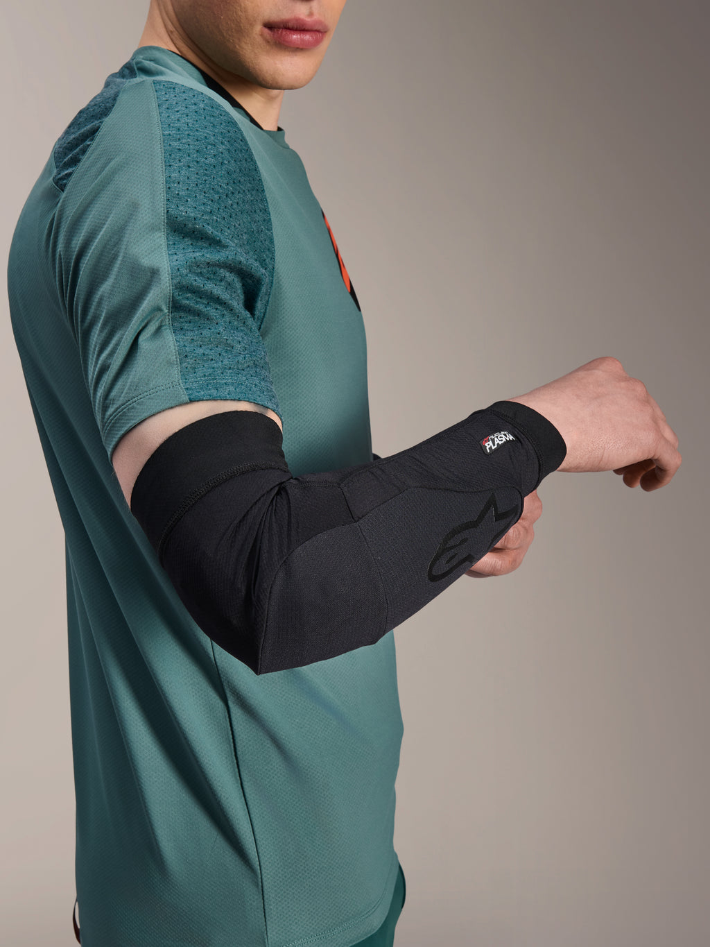 Alpinestars A-Motion Plasma Elbow Sleeve, protection de coude pour le cyclisme, noir, porté par un cycliste avec un maillot bleu sarcelle, arborant le logo Alpinestars et le marquage Nucleon Plasma, design épuré et respirant pour la protection VTT