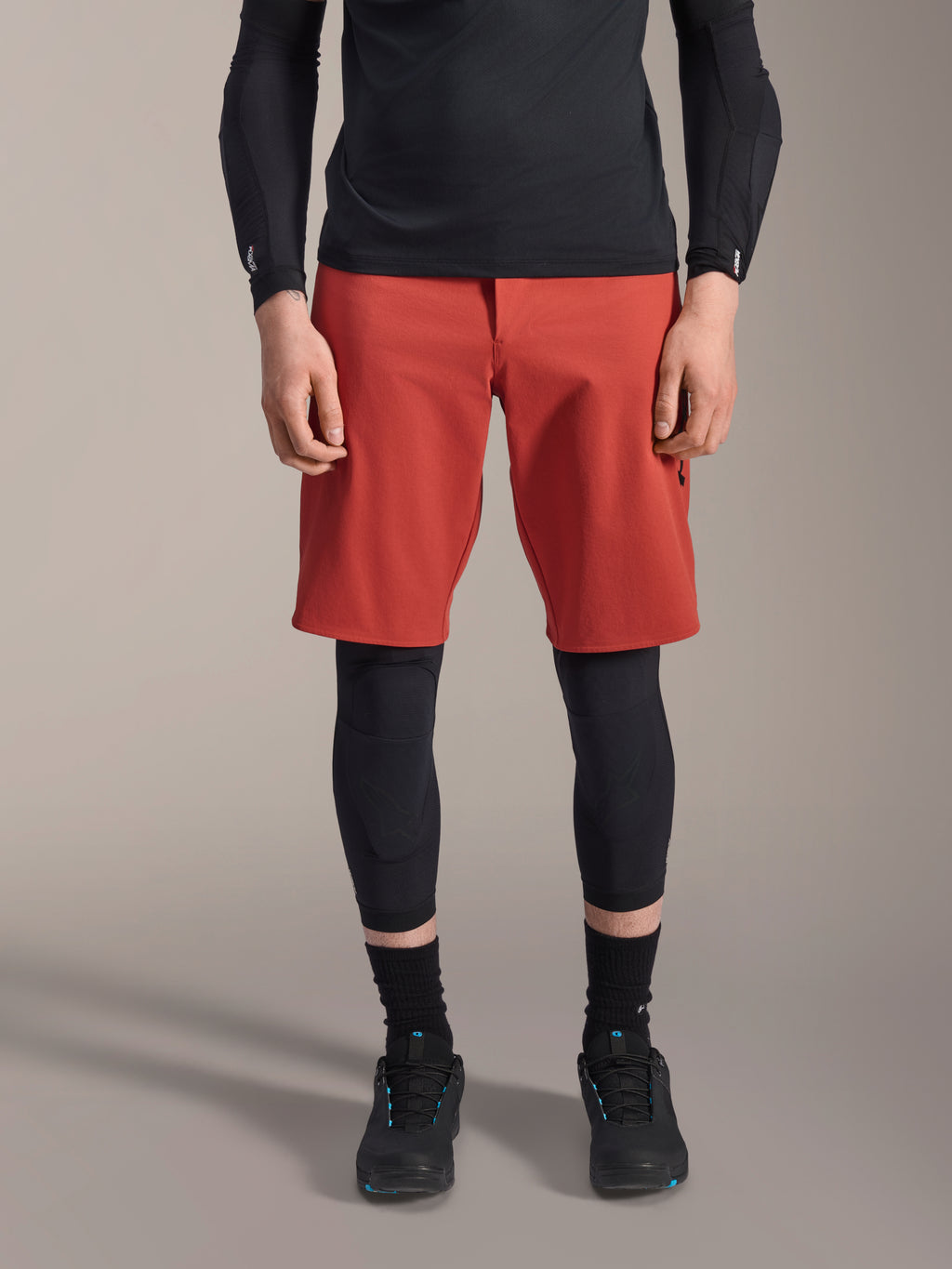 Alpinestars A-Motion Plasma Knee Sleeve, genouillère de VTT noire, portée avec un short rouge et un haut noir à manches longues, design ergonomique à profil mince, construction en maille légère pour le tout-terrain