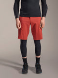 Alpinestars A-Motion Plasma Knee Sleeve, genouillère de VTT noire, portée avec un short rouge et un haut noir à manches longues, design ergonomique à profil mince, construction en maille légère pour le tout-terrain