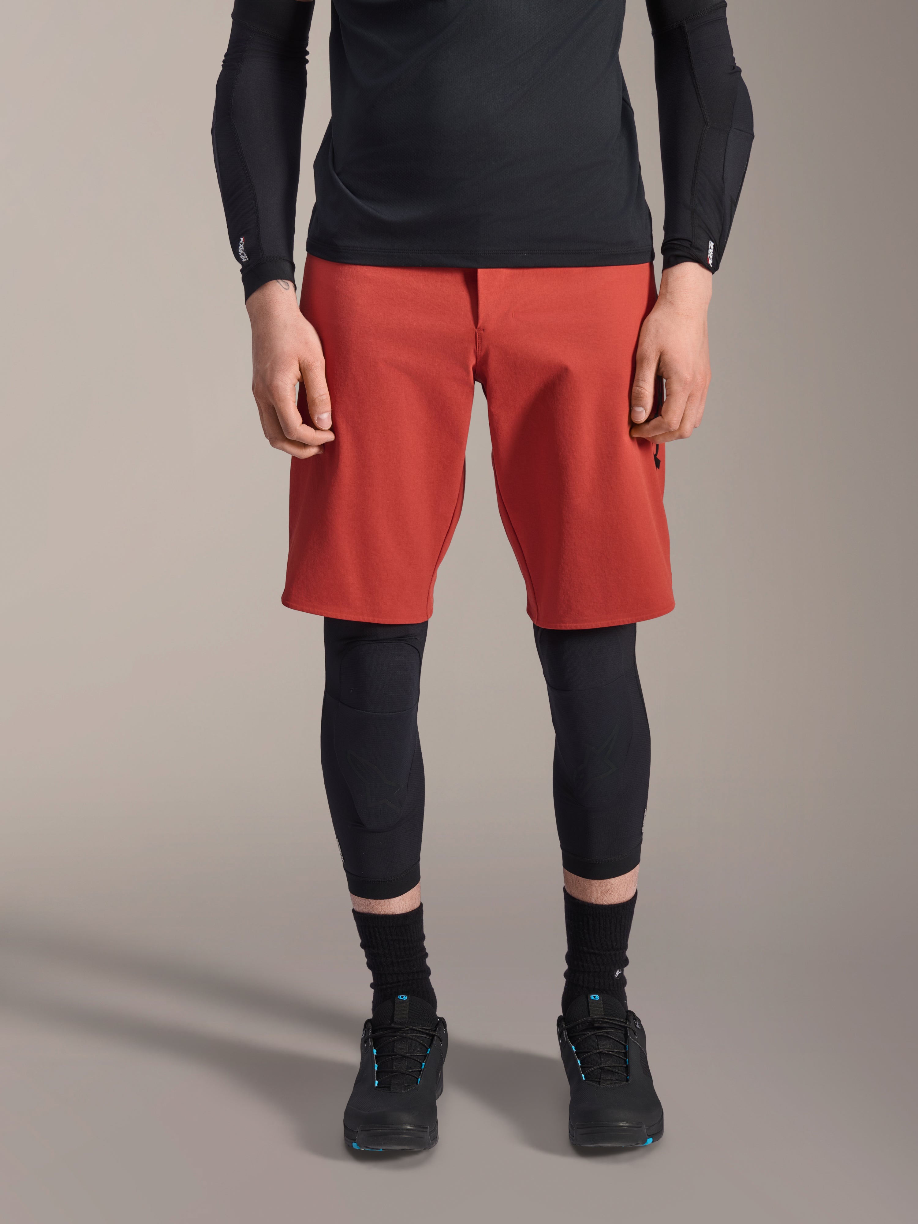 Alpinestars A-Motion Plasma Knee Sleeve, genouillère de VTT noire, portée avec un short rouge et un haut noir à manches longues, design ergonomique à profil mince, construction en maille légère pour le tout-terrain
