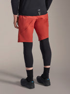 Alpinestars A-Motion Plasma Knee Sleeve, protection de genou VTT noire, porté avec un short de VTT rouge et des chaussures de cyclisme noires, vue arrière montrant le design discret à enfiler pour le cyclisme tout-terrain