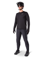 Cycliste de VTT portant le pantalon thermique Alpinestars A-Dura noir, avec un maillot à manches longues noir, un casque noir et des lunettes de soleil, logo Alpinestars argenté sur la cuisse gauche, conçu pour le trail par temps froid.