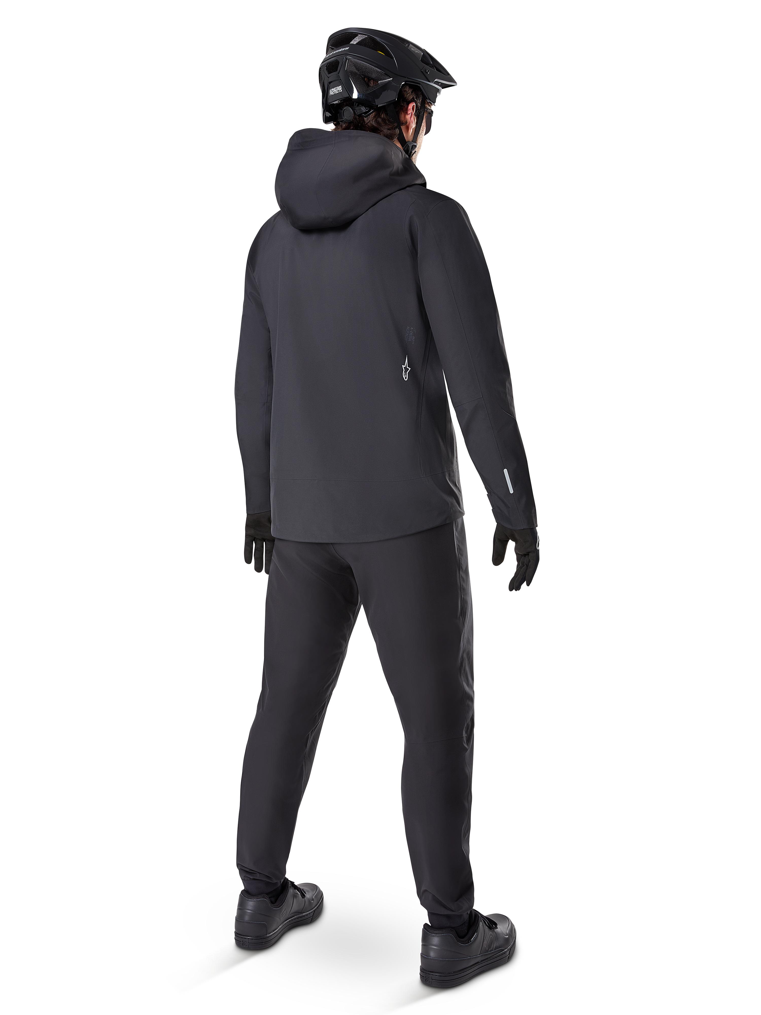 Pantalon imperméable Alpinestars A-Dura, pantalon de VTT, noir, vue de dos sur un cycliste portant une tenue de VTT noire complète avec une veste à capuche et un casque, équipement imperméable durable pour les sentiers boueux