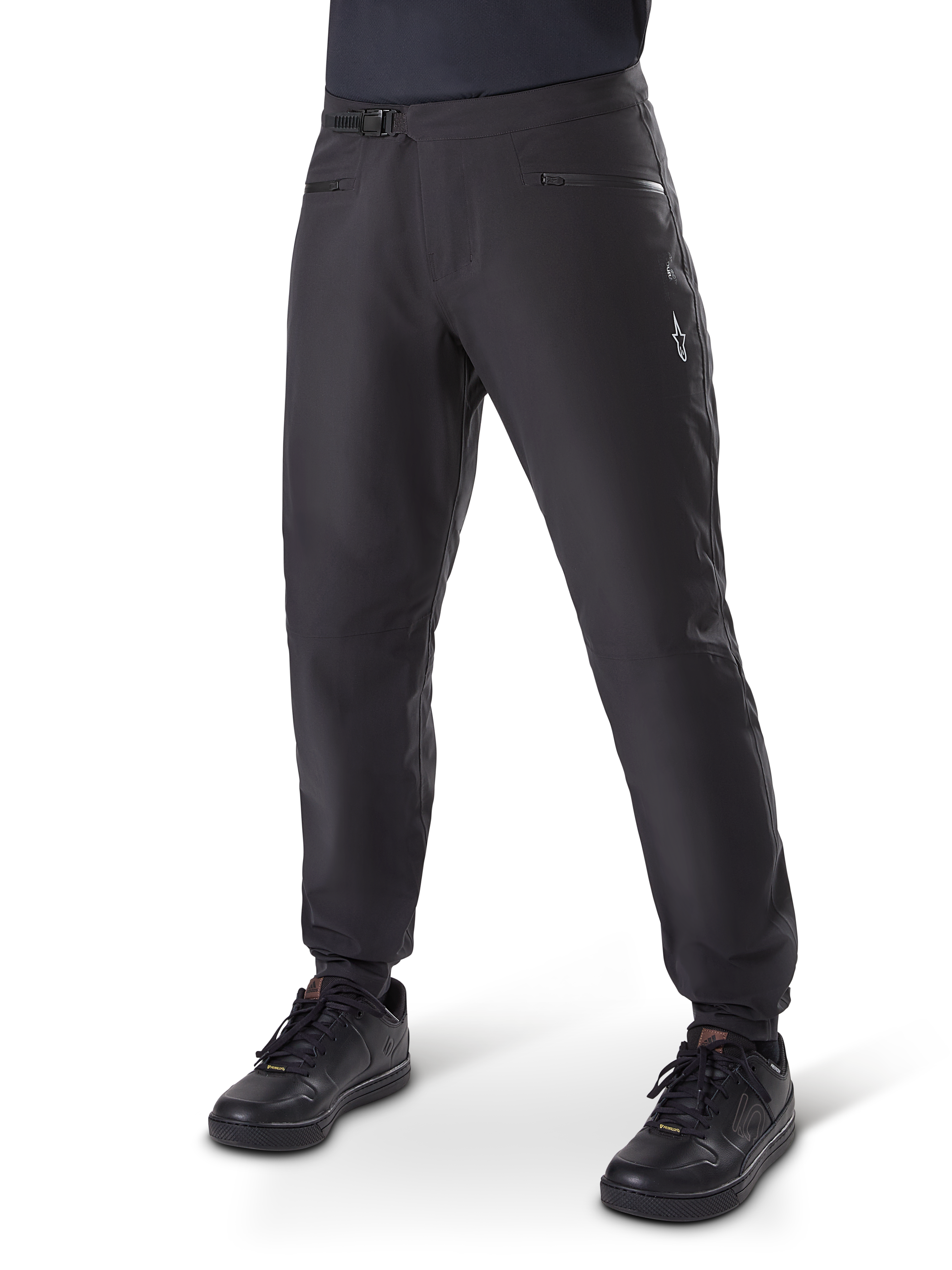 Pantalon imperméable Alpinestars A-Dura, pantalon de cyclisme VTT, noir, avec fermeture à cliquet à la taille, poches zippées et logo Astars blanc sur la cuisse, présenté porté avec des chaussures de vélo noires pour le trail par tous les temps