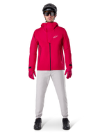 Pantalon imperméable Alpinestars A-Dura, pantalon de VTT, gris titane, porté avec une veste à capuche rouge vif, des gants rouges et un casque de VTT noir, équipement de cyclisme imperméable professionnel pour conditions de sentiers humides