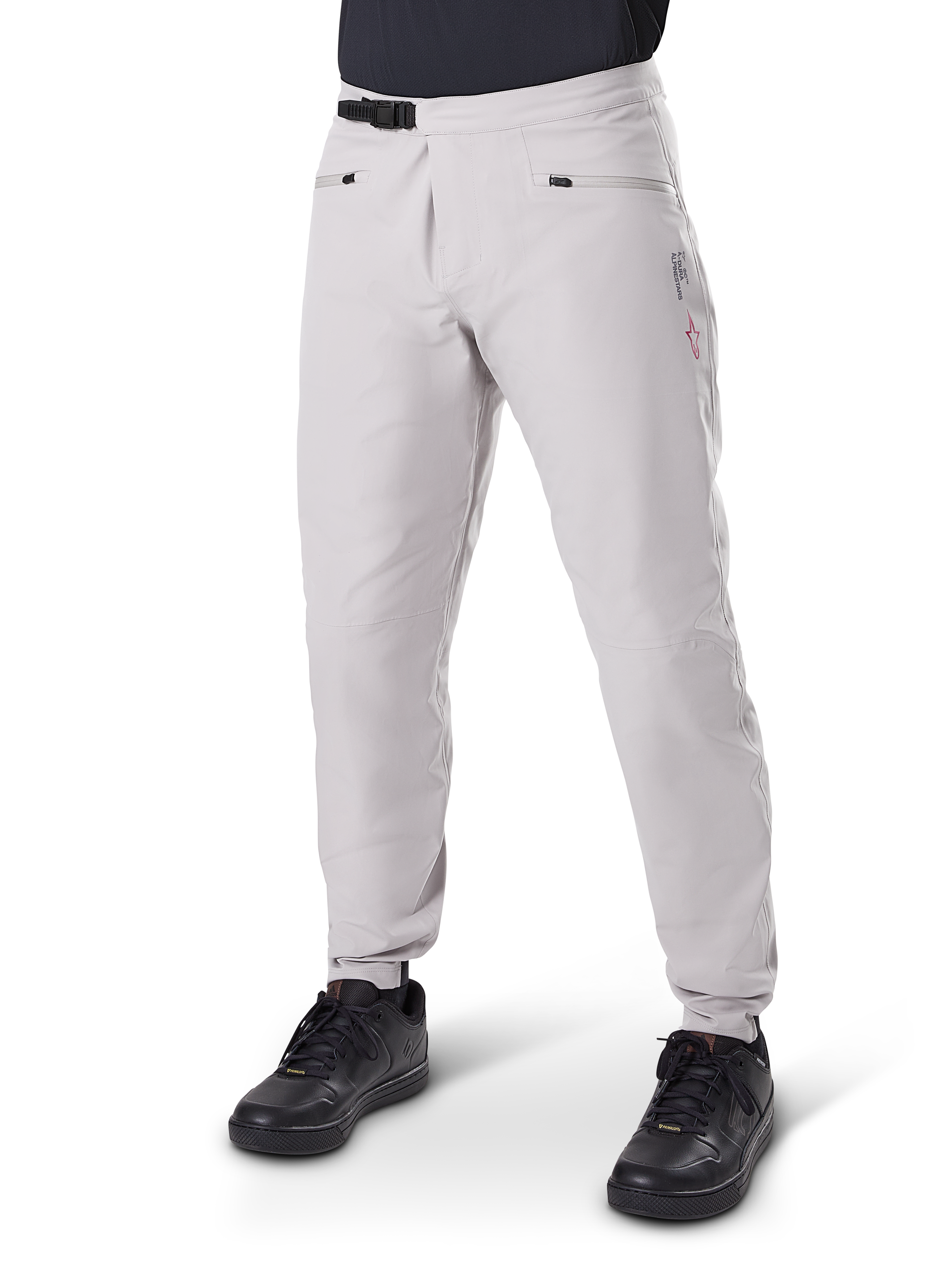 Pantalon imperméable Alpinestars A-Dura, pantalon de VTT, gris titane, doté d'une fermeture à cliquet noire à la taille et de poches zippées, jambes fuselées avec poignets élastiqués, porté avec des chaussures noires, construction imperméable 3L durable pour le cyclisme tout-terrain
