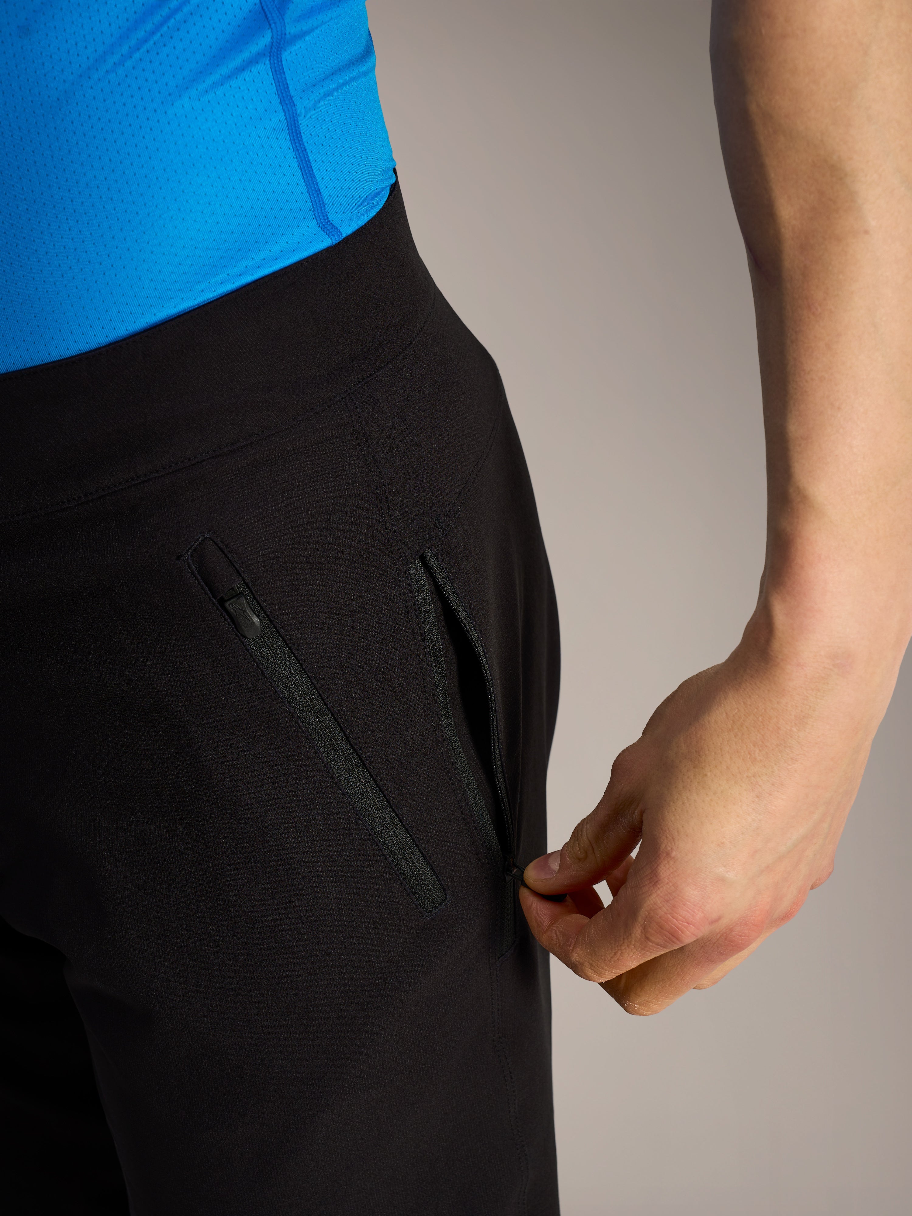 Short VTT Alpinestars A-Dura Ride noir, gros plan d'une main ouvrant une poche latérale zippée sécurisée.