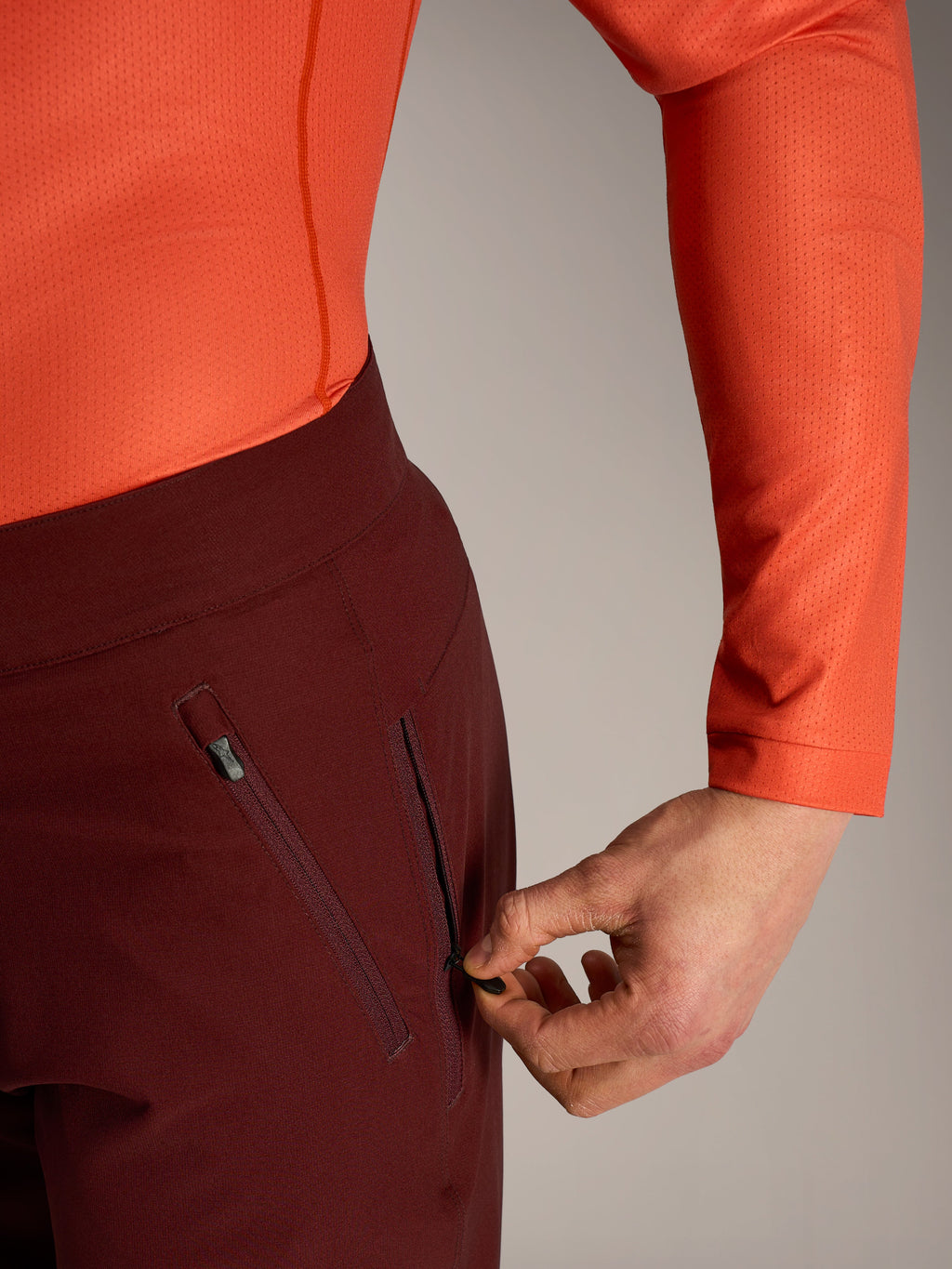 Shorts Alpinestars A-Dura Ride bordeaux, détail d'une main ouvrant la poche latérale zippée doublée de mesh.