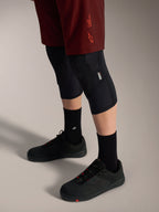 Shorts Alpinestars A-Dura Ride bordeaux, coupe extensible et logo signature, portés avec genouillères et chaussures noires.