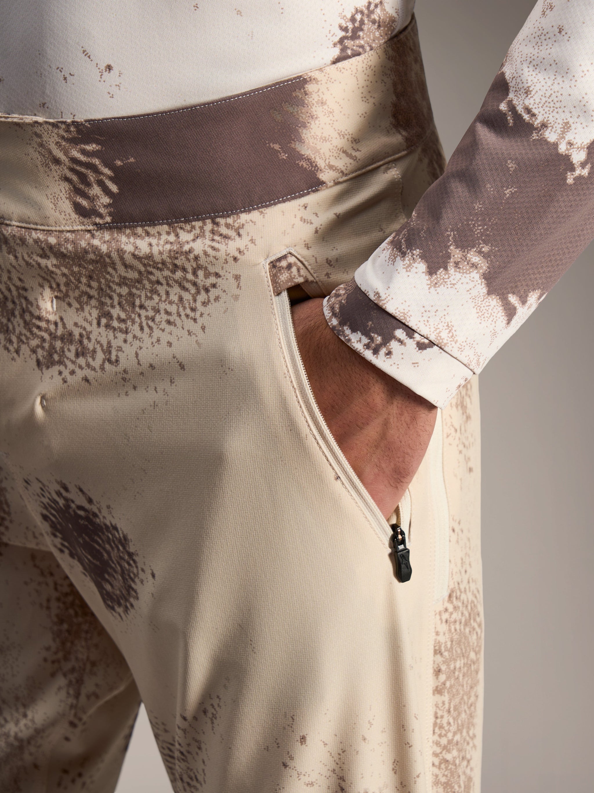 Alpinestars A-Dura Ride Shorts in Sand Camo, showing a zippered side pocket and durable 4-way stretch MTB fabric.