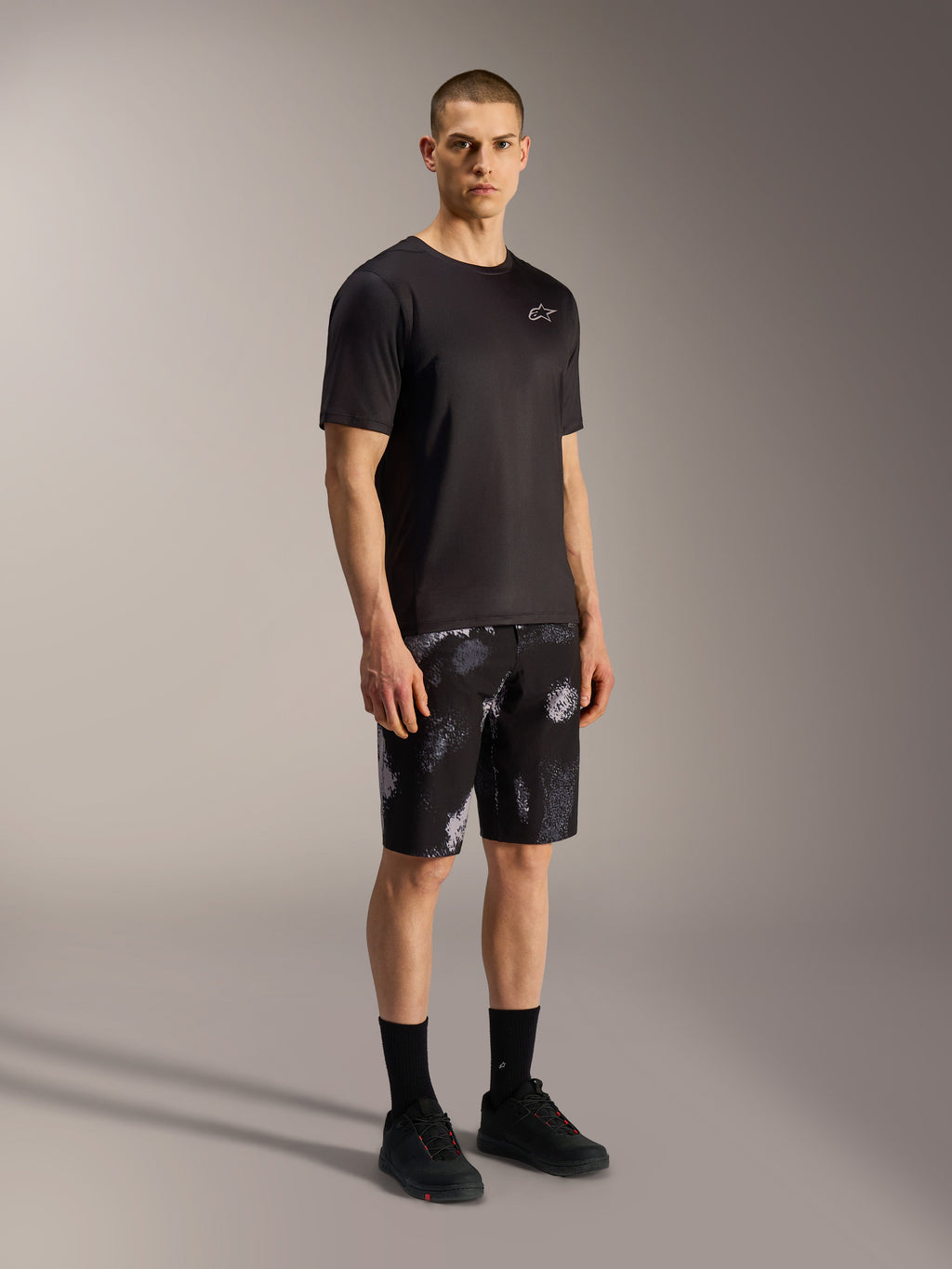 Short Alpinestars A-Dura Ride Black Camo, motif camouflage gris, porté avec un maillot et des chaussures de VTT noirs.