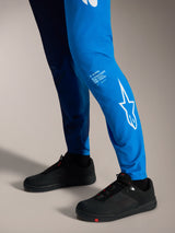 Pantalons A-Supra Elite bleu vif délavé, logo Astars blanc sur le bas de la jambe et chaussures de VTT noires.