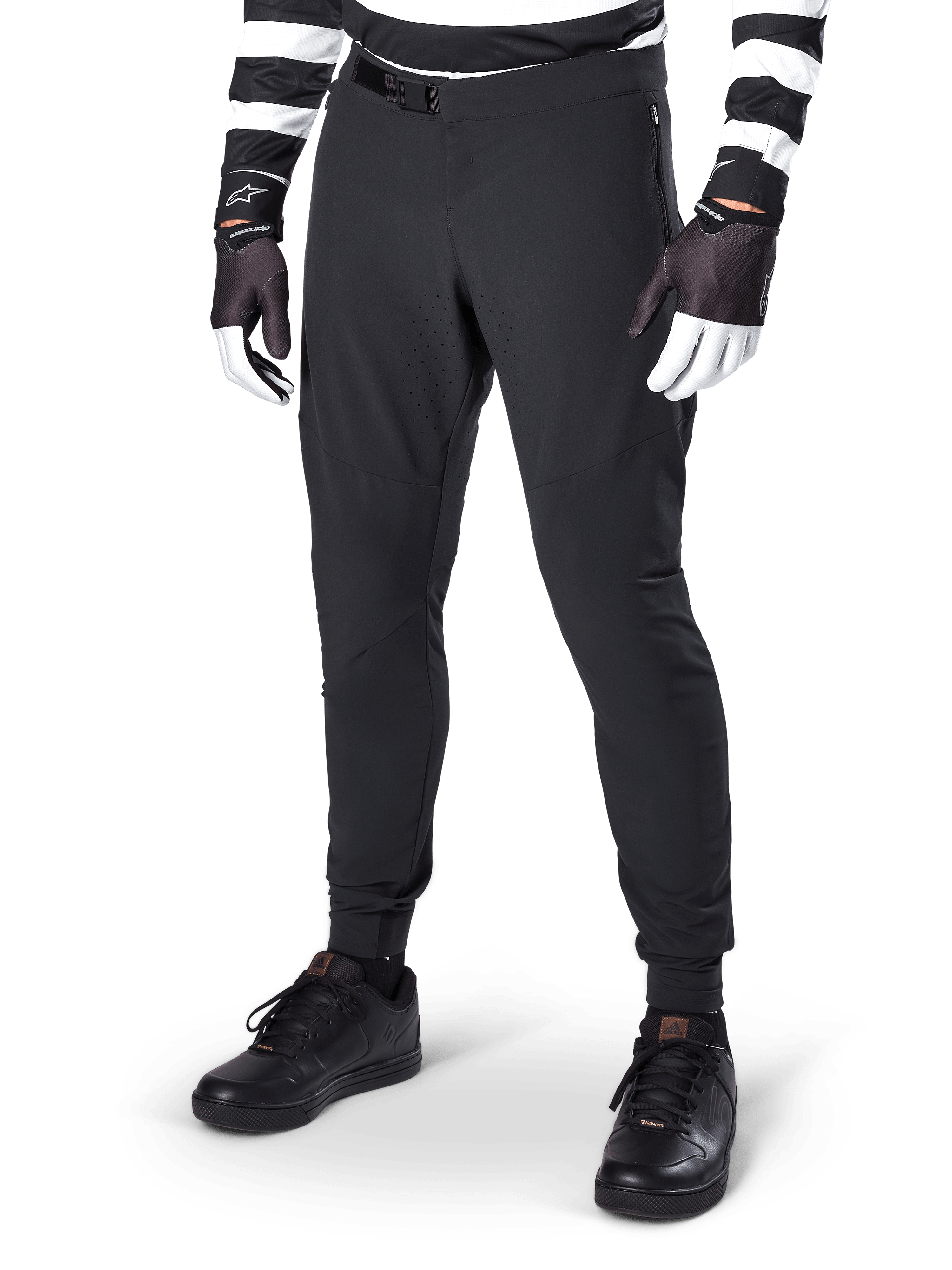 Alpinestars A-Aria Elite Pants, pantalon de VTT noir, doté de ventilations découpées au laser sur les cuisses et d'une fermeture à boucle magnétique, porté avec un maillot et des gants rayés noir et blanc, équipement de VTT de performance pour le cyclisme tout-terrain