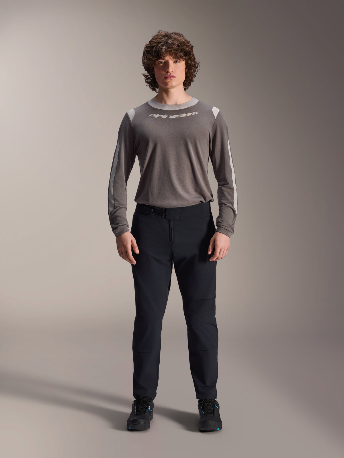 Pantalon Alpinestars A-Dura Elite, pantalon de VTT noir, vêtement technique de cyclisme à coupe régulière, porté avec un maillot gris à manches longues et des chaussures noires, construction durable en Cordura® pour la pratique tout-terrain
