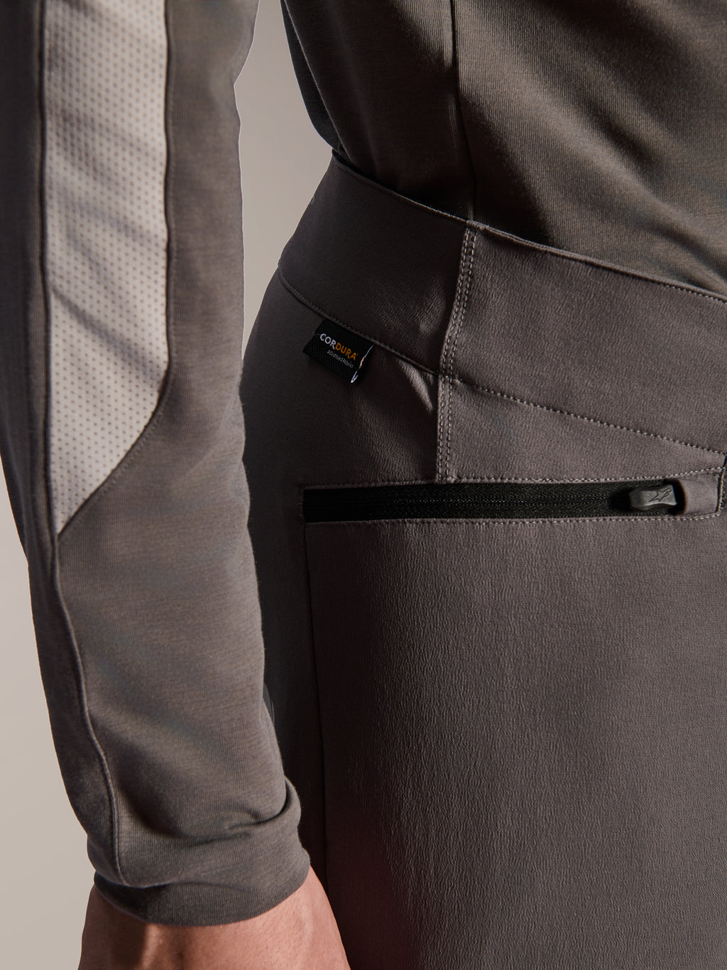 Pantalon Alpinestars A-Dura Elite, pantalon de VTT gris foncé, gros plan sur la poche latérale zippée et l'étiquette en tissu Cordura, textile extensible 4 directions durable pour la performance tout-terrain