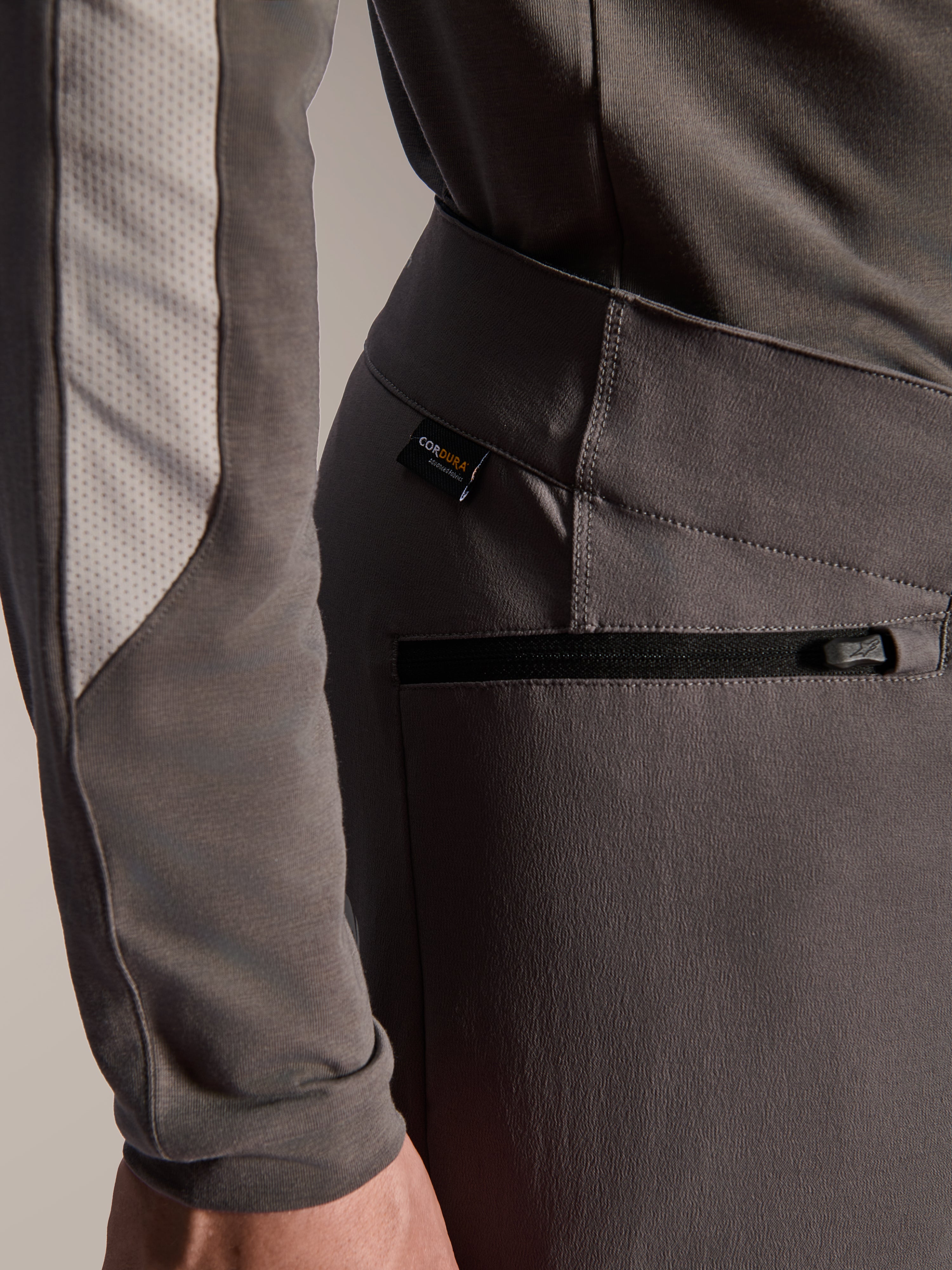 Pantalon Alpinestars A-Dura Elite, pantalon de VTT gris foncé, gros plan sur la poche latérale zippée et l'étiquette en tissu Cordura, textile extensible 4 directions durable pour la performance tout-terrain