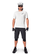 Male mountain biker wearing Alpinestars A-Aria Shorts, Black, paired with a white performance jersey, white helmet, and black knee protectors, professional off-road cycling gear in a full-body front view