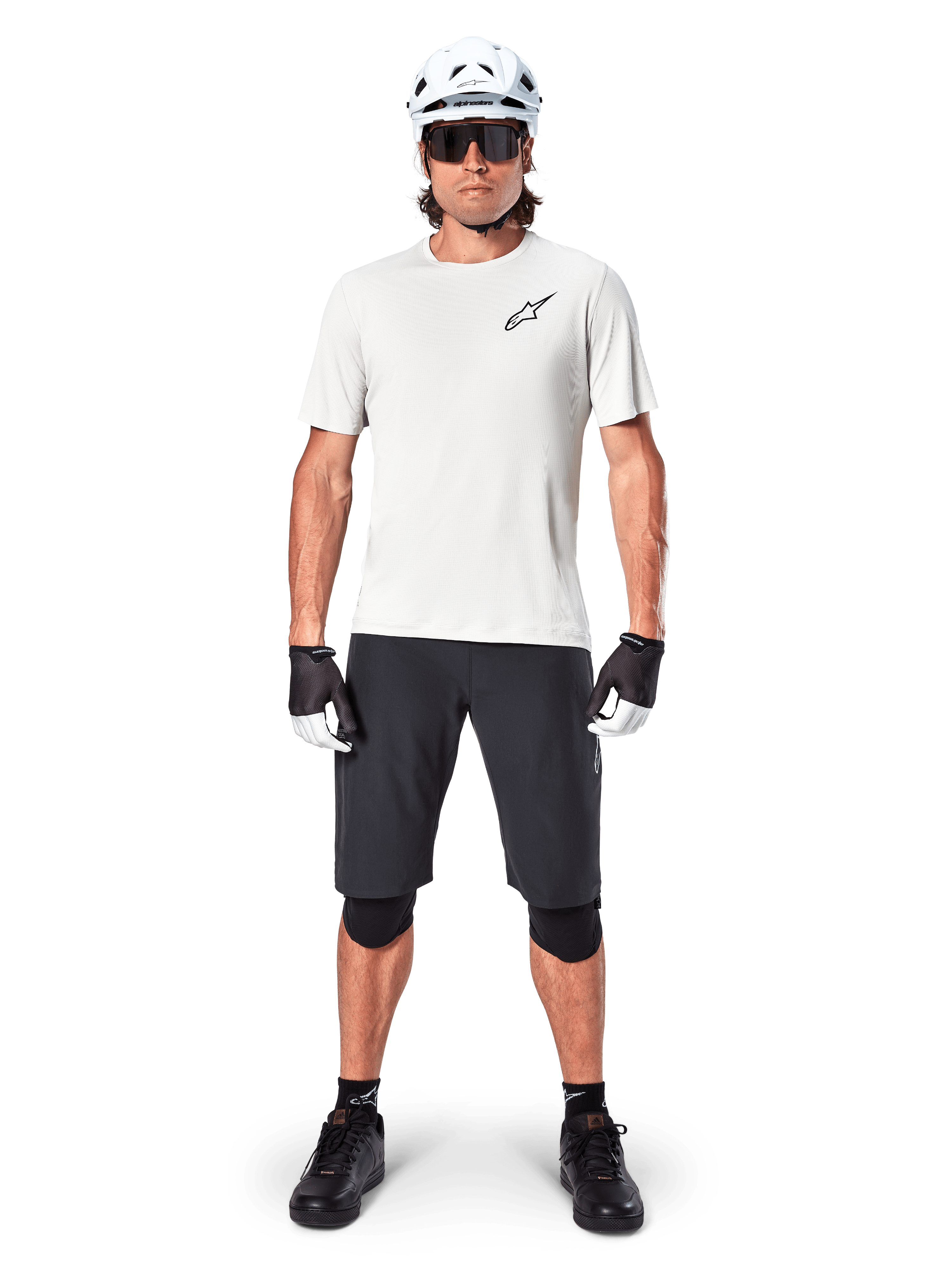 Male mountain biker wearing Alpinestars A-Aria Shorts, Black, paired with a white performance jersey, white helmet, and black knee protectors, professional off-road cycling gear in a full-body front view