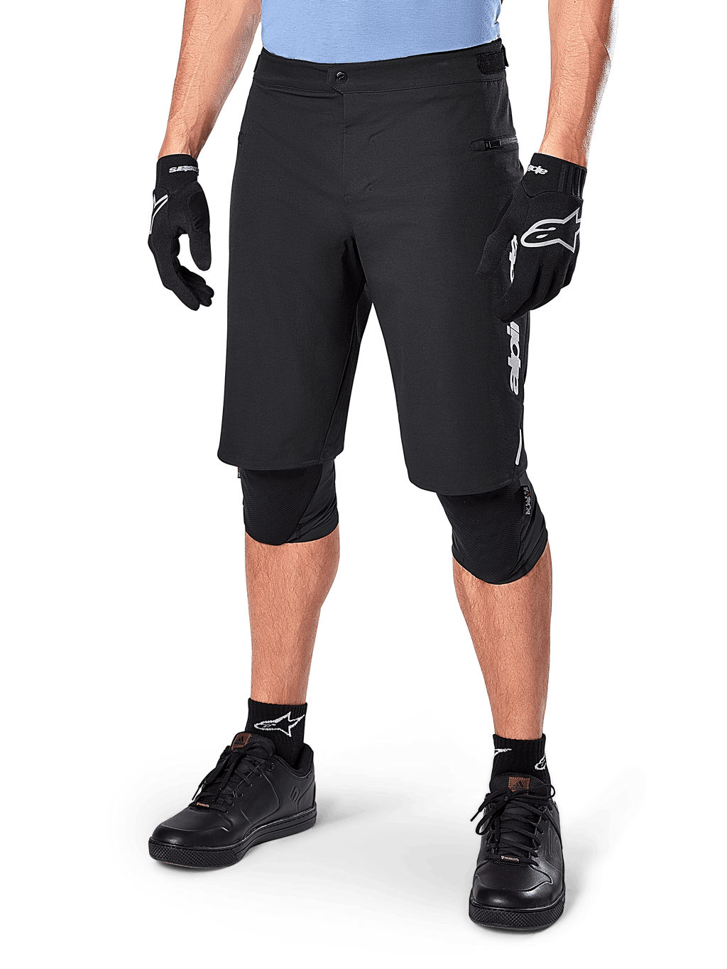 Alpinestars A-Dura Elite Shorts, Black MTB Mountain Biking Shorts, worn with light blue shirt and black knee protection, featuring a secure snap closure and zippered pocket, paired with black cycling shoes and gloves for a complete off-road outfit.
