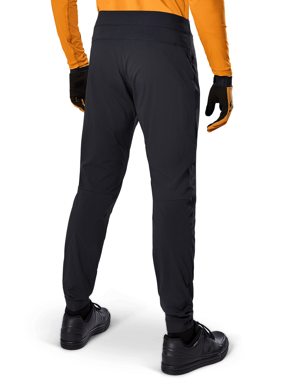 Pantalon Alpinestars A-Dura, pantalon de VTT noir, vue arrière, porté avec un maillot orange à manches longues et des gants noirs, doté de manchettes élastiquées et d'un matériau textile durable pour le VTT