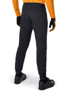 Pantalon Alpinestars A-Dura, pantalon de VTT noir, vue arrière, porté avec un maillot orange à manches longues et des gants noirs, doté de manchettes élastiquées et d'un matériau textile durable pour le VTT