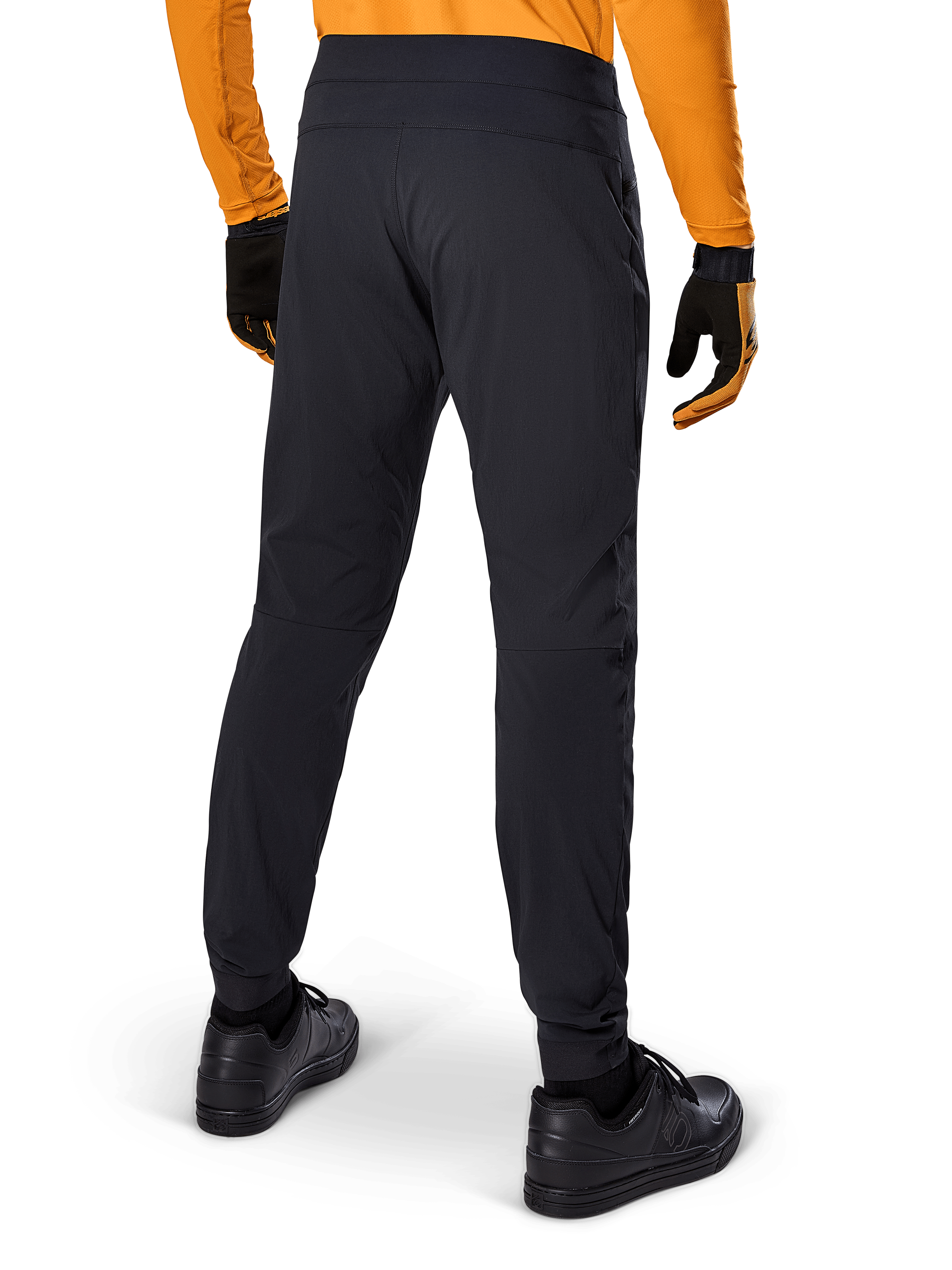 Pantalon Alpinestars A-Dura, pantalon de VTT noir, vue arrière, porté avec un maillot orange à manches longues et des gants noirs, doté de manchettes élastiquées et d'un matériau textile durable pour le VTT