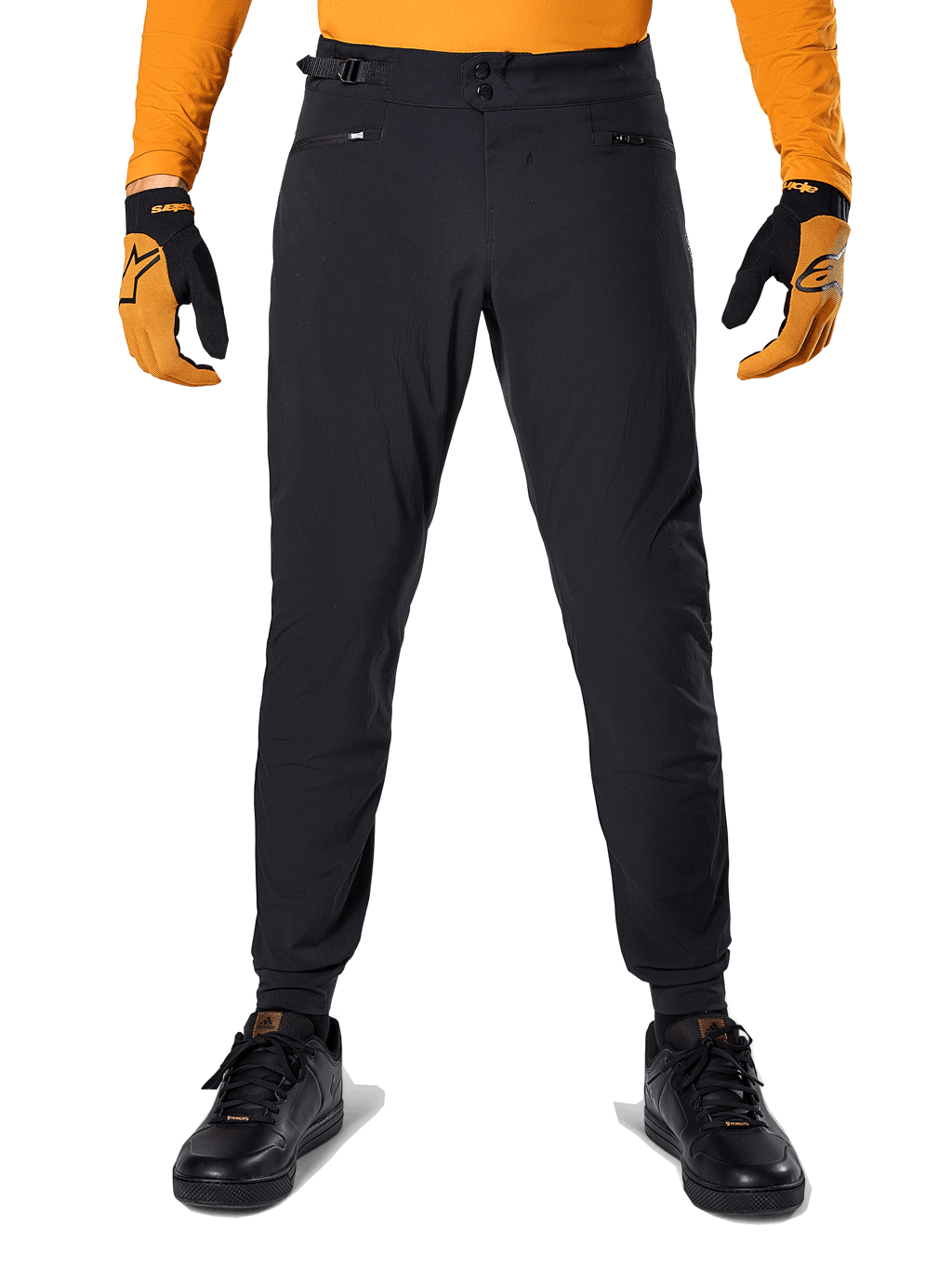 Pantalon Alpinestars A-Dura, pantalon de VTT, noir, porté avec un maillot orange à manches longues et des gants noir et orange, doté d'une double fermeture à pression et de réglages latéraux à la taille, textile durable pour le cyclisme tout-terrain