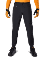 Pantalon Alpinestars A-Dura, pantalon de VTT, noir, porté avec un maillot orange à manches longues et des gants noir et orange, doté d'une double fermeture à pression et de réglages latéraux à la taille, textile durable pour le cyclisme tout-terrain