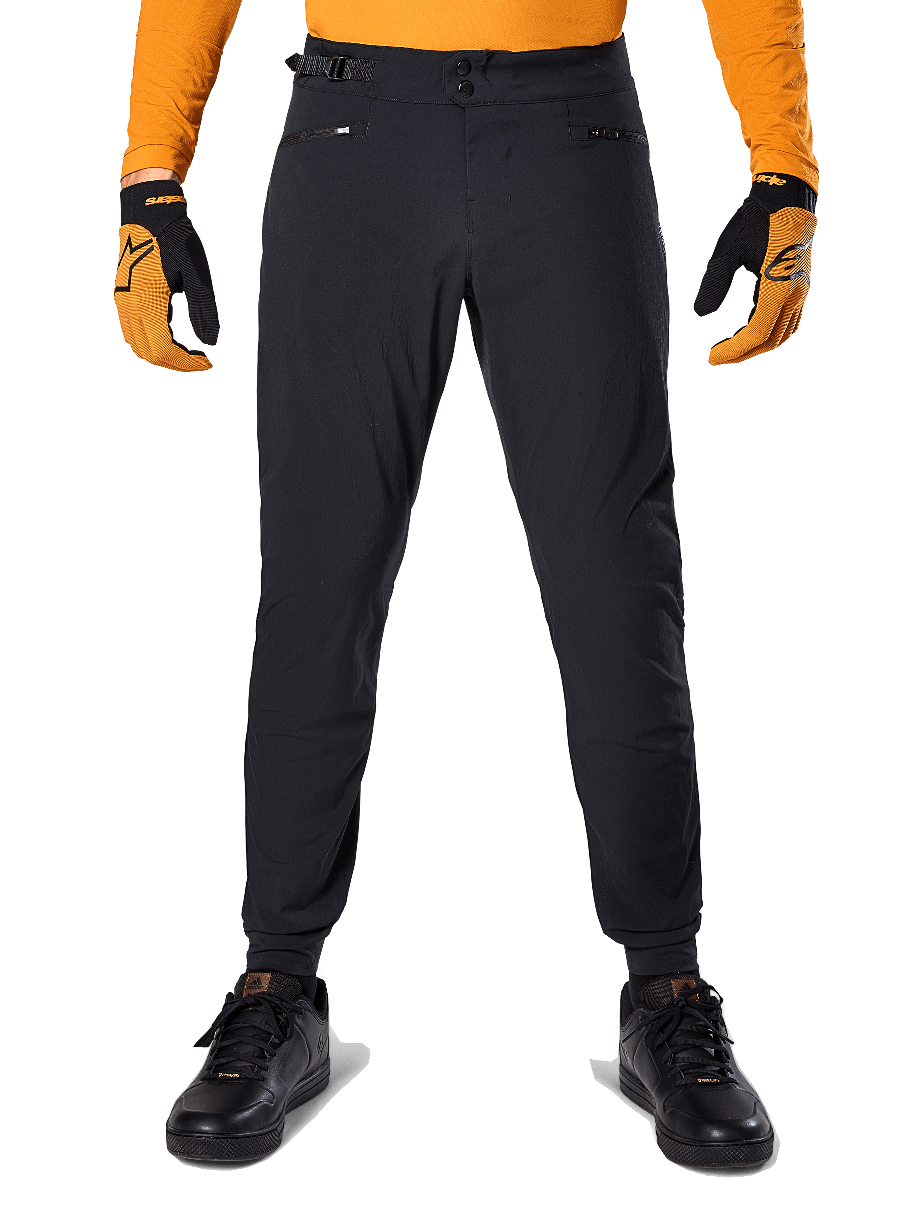 Pantalon Alpinestars A-Dura, pantalon de VTT, noir, porté avec un maillot orange à manches longues et des gants noir et orange, doté d'une double fermeture à pression et de réglages latéraux à la taille, textile durable pour le cyclisme tout-terrain