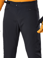 Pantalon Alpinestars A-Dura, pantalon de cyclisme VTT noir, vue rapprochée présentant la double fermeture à pression à la taille, l'ajusteur latéral réglable et les poches zippées, porté avec un maillot et des gants orange