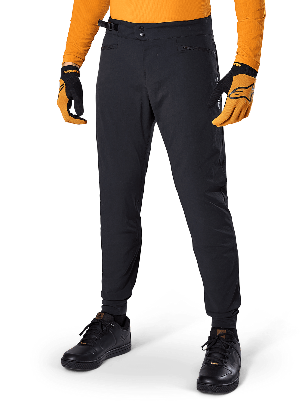 Alpinestars A-Dura Pants, pantalon de VTT, noir, serrages latéraux à la taille et poches zippées, porté avec un maillot et des gants orange, coupe régulière sportive pour la pratique du VTT