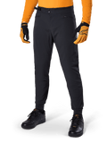Alpinestars A-Dura Pants, pantalon de VTT, noir, serrages latéraux à la taille et poches zippées, porté avec un maillot et des gants orange, coupe régulière sportive pour la pratique du VTT
