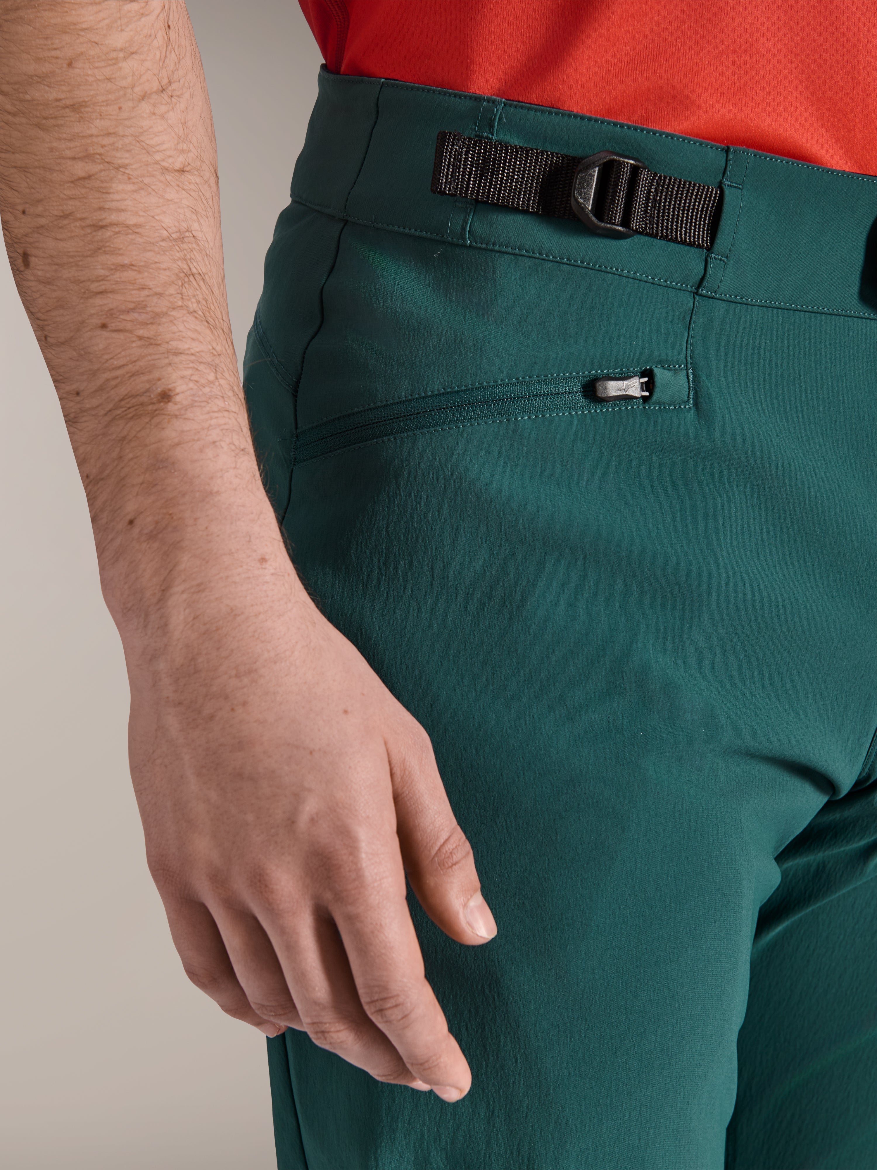 Gros plan sur le pantalon Alpinestars A-Dura en vert Dark Pine, présentant l'ajusteur de taille latéral et une poche zippée doublée de maille, un vêtement de VTT résistant pour la pratique sur sentiers tout-terrain.