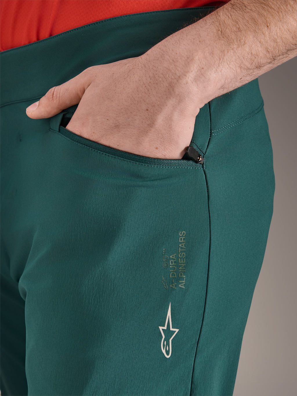 Pantalon Alpinestars A-Dura vert Dark Pine, gros plan d'une poche zippée avec une main, logo Alpinestars blanc et marquage sur la cuisse, pantalon de VTT durable