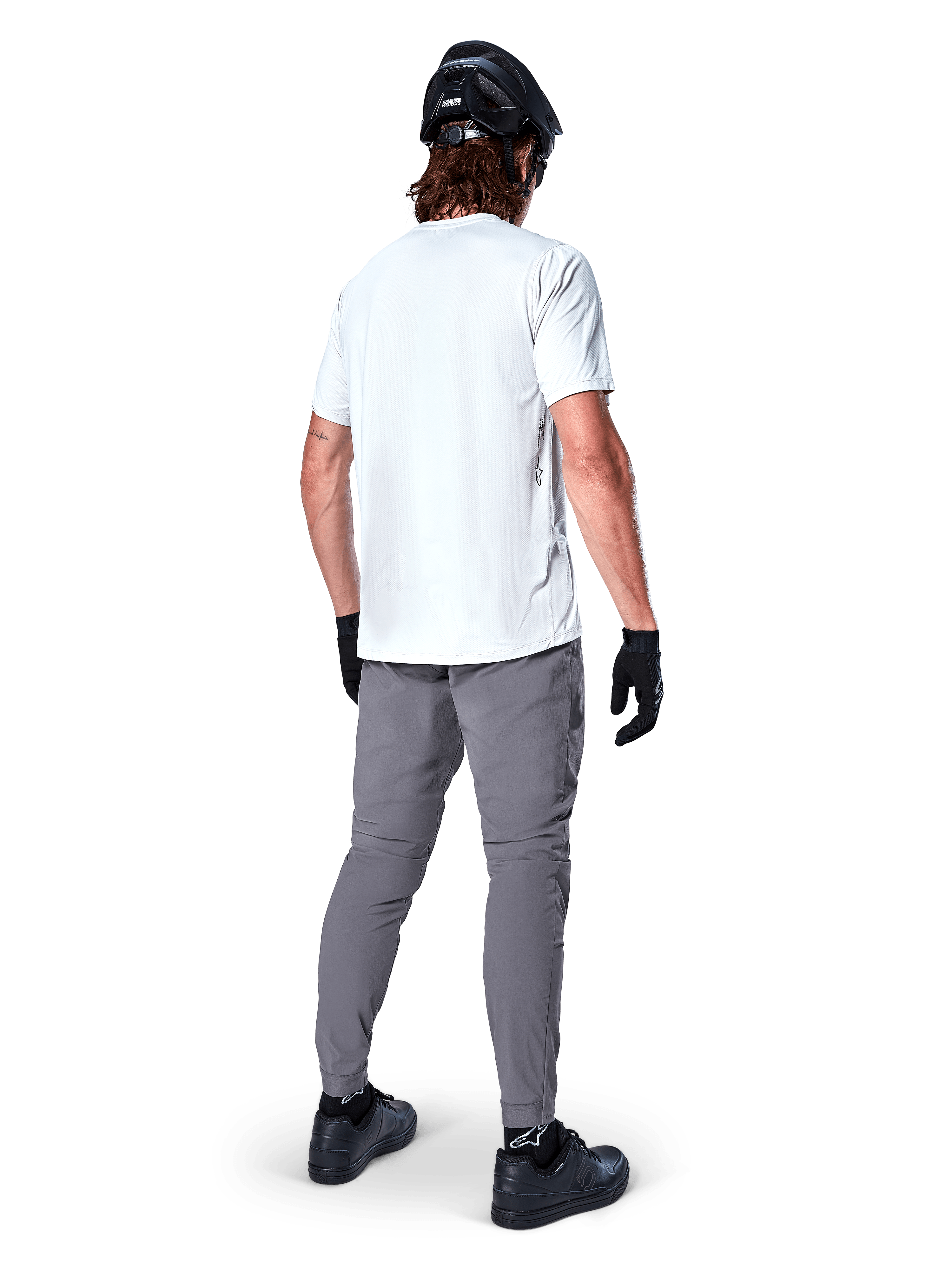 Alpinestars A-Dura Pants, Dark Gray Mountain Bike Pants shown from the back, worn with a white short-sleeve t-shirt, black MTB helmet, black gloves and shoes, regular fit design with elasticated cuffs, durable off-road cycling gear