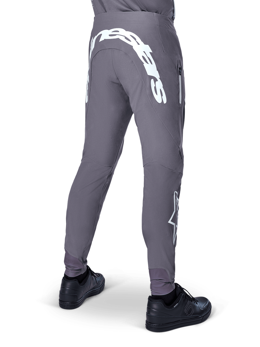 Pantalon Alpinestars A-Supra Race, pantalon de VTT, gris foncé, vue arrière porté avec des chaussures noires, doté d'un grand lettrage Alpinestars blanc à l'arrière et d'un logo étoile sur la jambe, poche zippée, tissu extensible haute performance pour la course de VTT