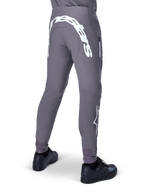 Pantalon Alpinestars A-Supra Race, pantalon de VTT, gris foncé, vue arrière porté avec des chaussures noires, doté d'un grand lettrage Alpinestars blanc à l'arrière et d'un logo étoile sur la jambe, poche zippée, tissu extensible haute performance pour la course de VTT