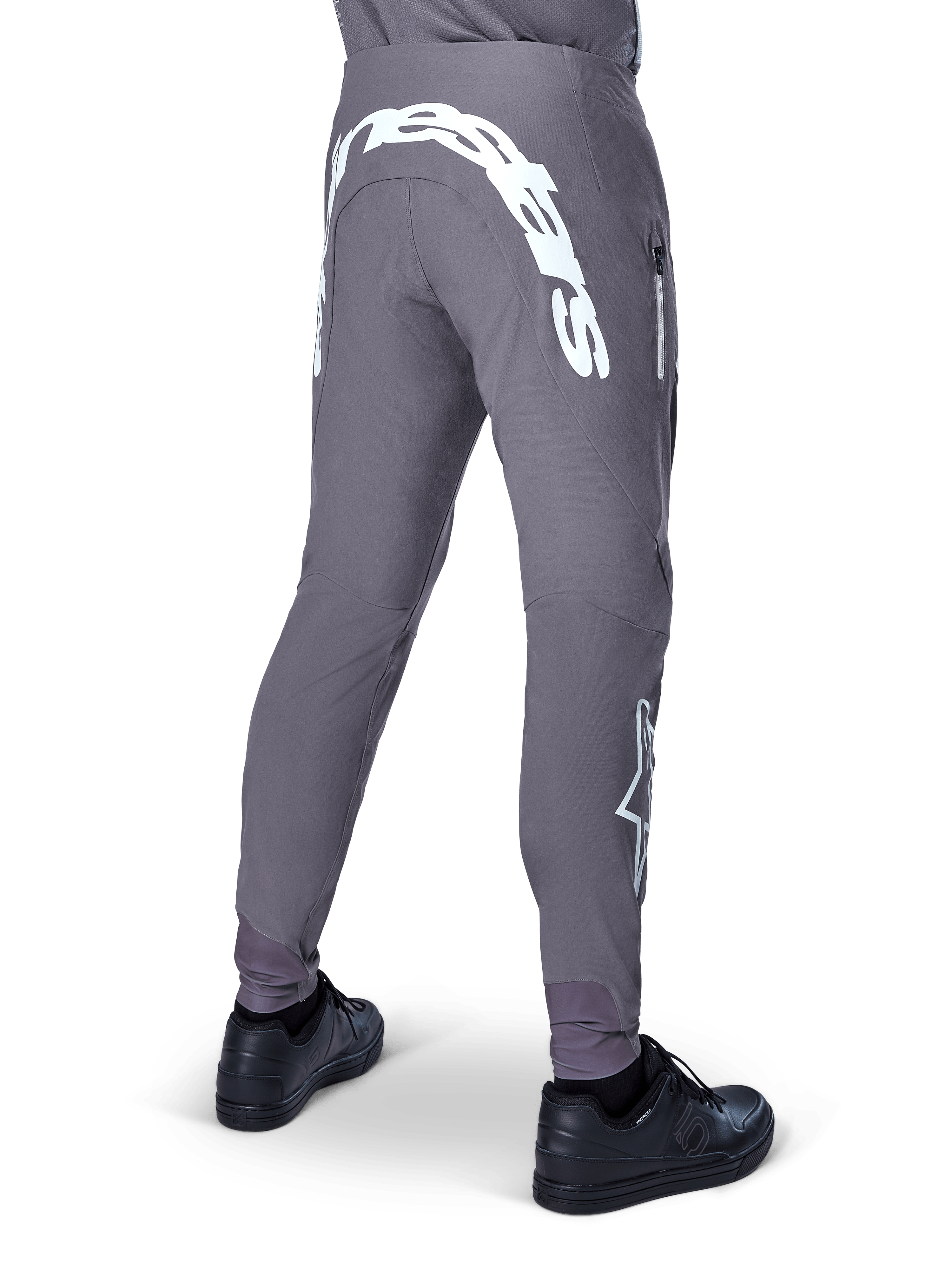 Pantalon Alpinestars A-Supra Race, pantalon de VTT, gris foncé, vue arrière porté avec des chaussures noires, doté d'un grand lettrage Alpinestars blanc à l'arrière et d'un logo étoile sur la jambe, poche zippée, tissu extensible haute performance pour la course de VTT