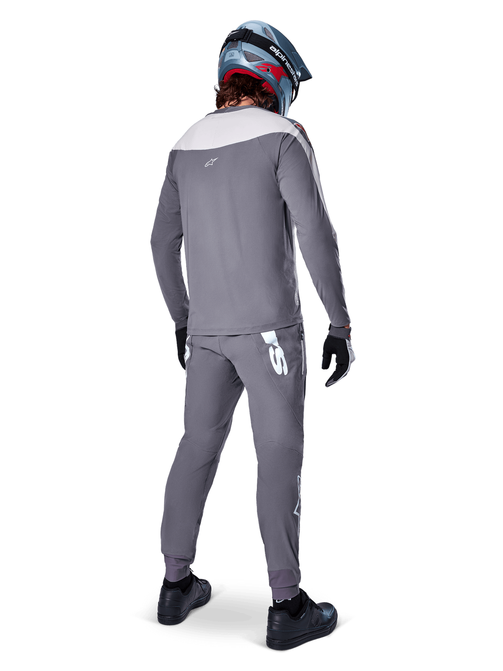 Alpinestars A-Supra Race Pants, gris foncé, cycliste de VTT vu de dos portant une tenue de course complète, maillot gris à manches longues, pantalon gris foncé avec logo blanc d'inspiration MX sur l'empiècement arrière, casque gris et bleu, chaussures noires, conçu pour la performance en VTT