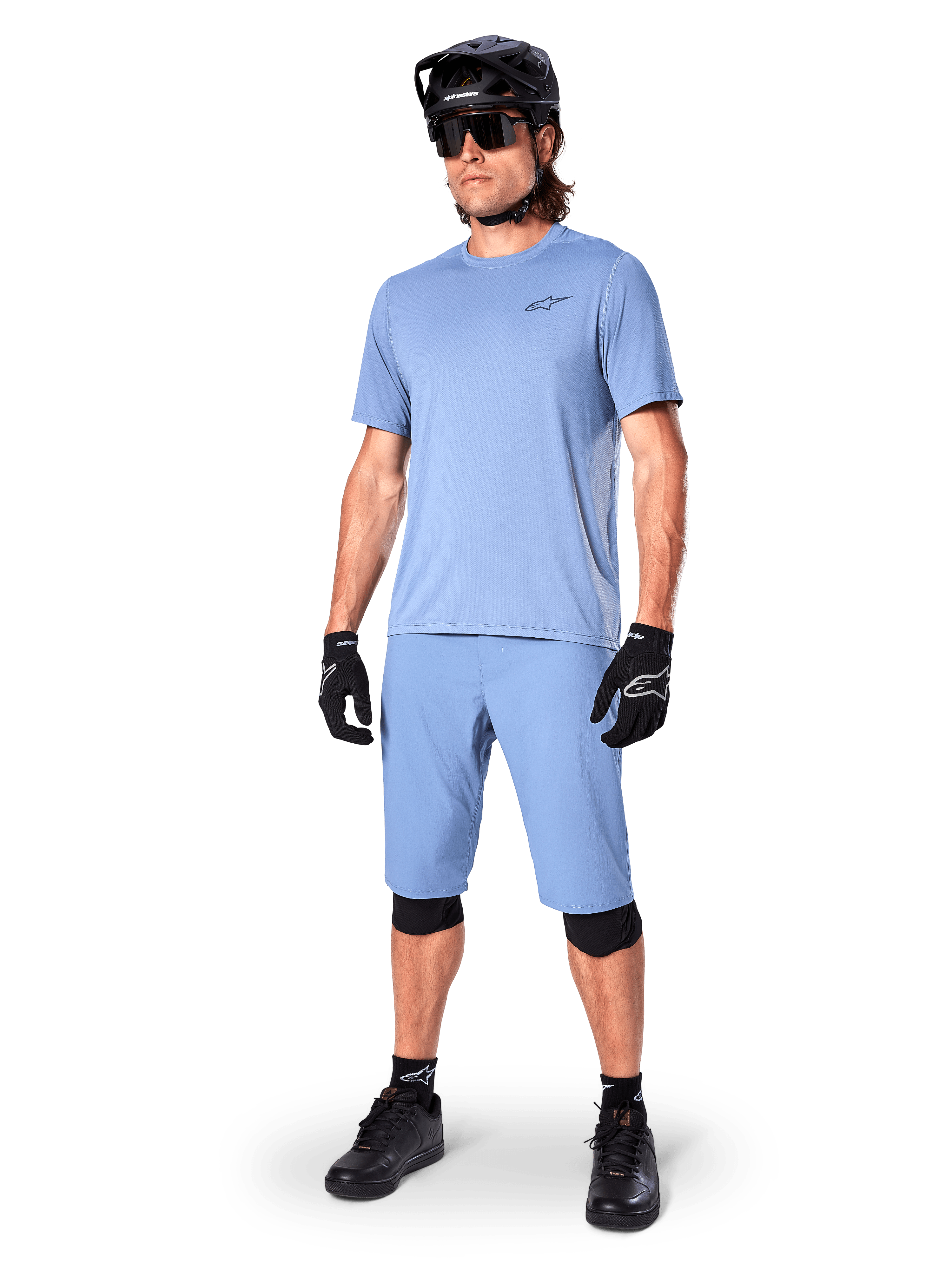 Model wearing Alpinestars A-Dura Shorts in Infinity Blue, matching light blue short-sleeve jersey, black MTB helmet, sunglasses, and black gloves, complete mountain biking outfit for trail riding