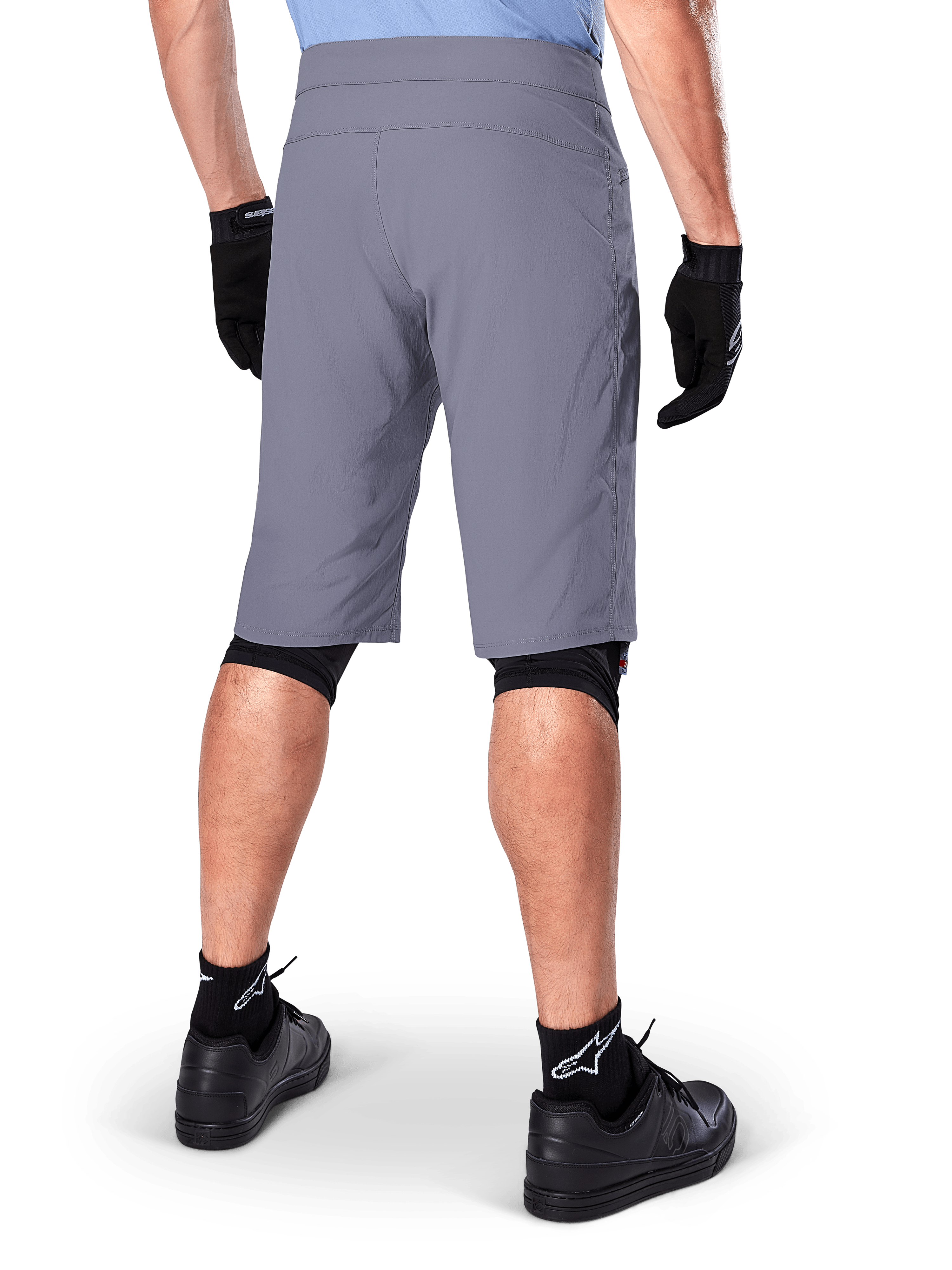 Short Alpinestars A-Dura, short de VTT gris foncé, vue arrière portée par un cycliste avec gants noirs, genouillères noires et chaussettes noires à logo Alpinestars, construction durable pour le cyclisme tout-terrain
